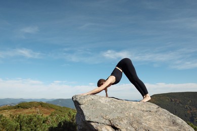 Beautiful young woman practicing yoga on rock in mountains