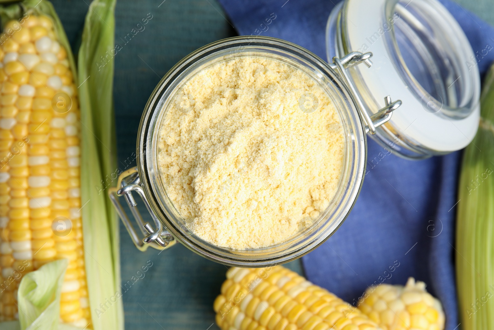 Photo of Corn flour in glass jar and fresh cobs on blue wooden table, flat lay