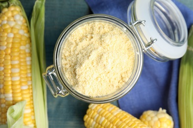 Photo of Corn flour in glass jar and fresh cobs on blue wooden table, flat lay