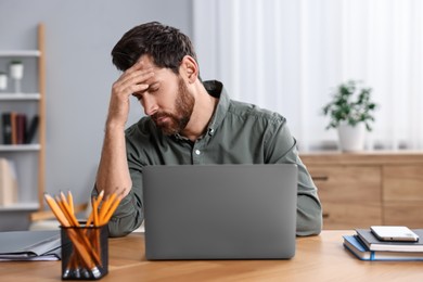 Photo of Tired man suffering from headache at workplace in office