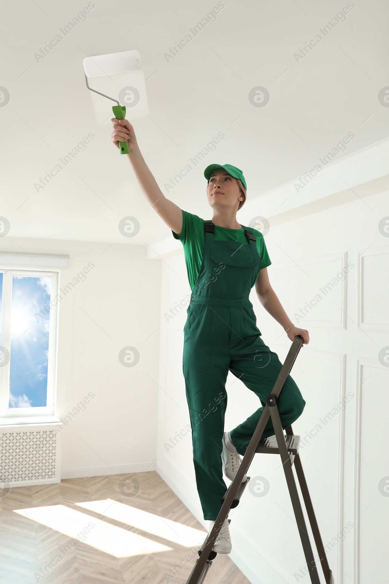 Photo of Worker painting ceiling with white dye indoors