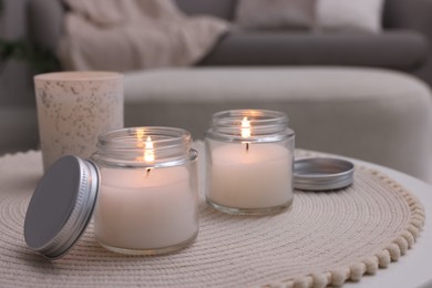 Burning candles in jars on white table indoors, space for text