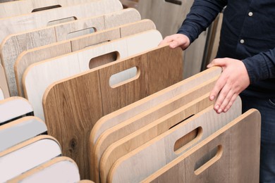 Photo of Man choosing wooden flooring among different samples in shop, closeup