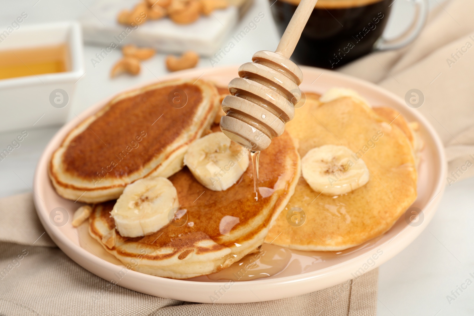 Photo of Pouring honey onto pancakes with banana on table, closeup