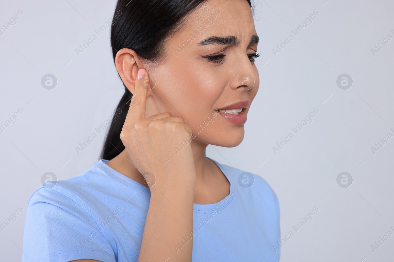 Photo of Young woman suffering from ear pain on light grey background, closeup