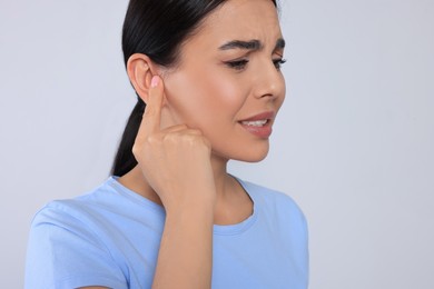 Young woman suffering from ear pain on light grey background, closeup