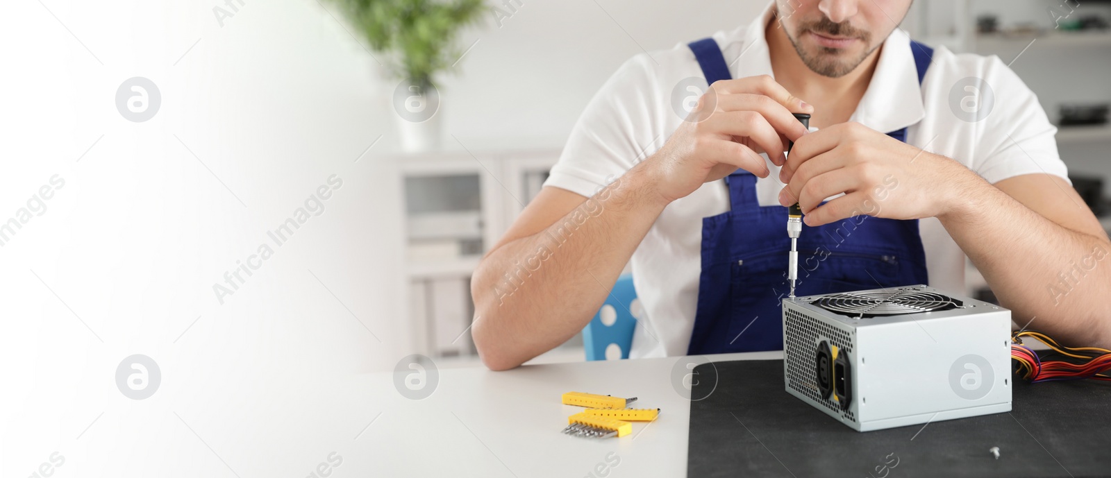 Image of Male technician repairing power supply unit at table indoors, space for text. Banner design