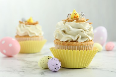 Photo of Tasty Easter cupcakes with vanilla cream and candies on white marble table