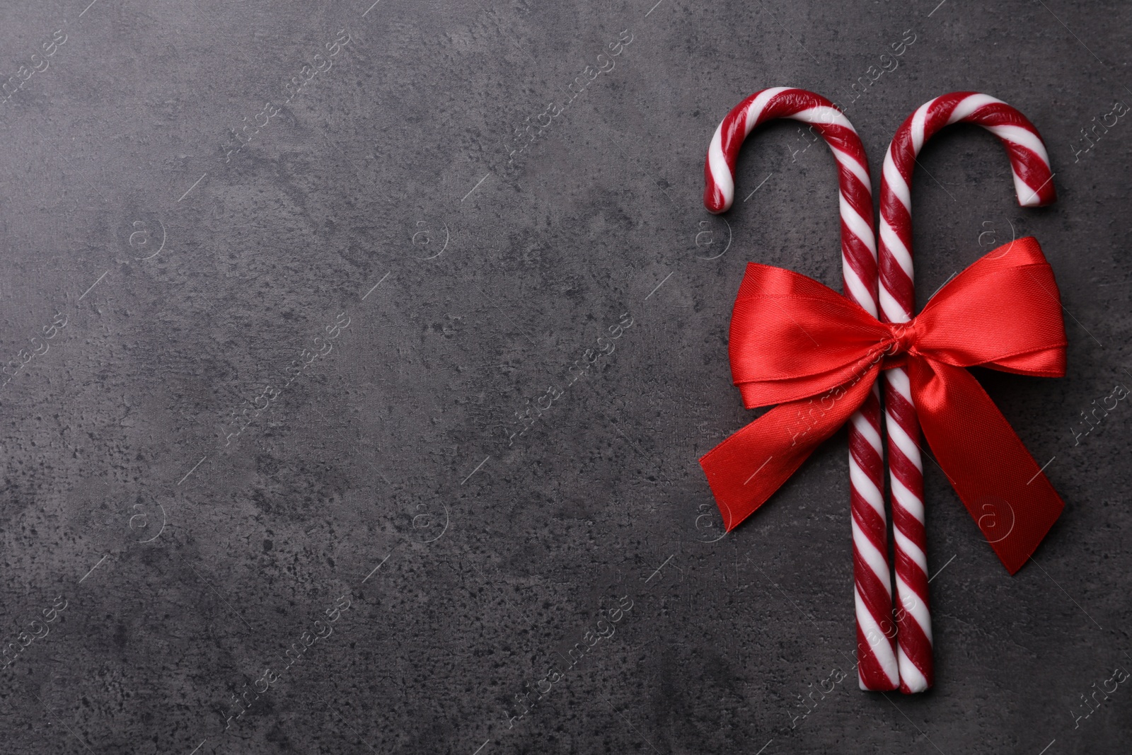 Photo of Sweet Christmas candy canes with red bow on grey background, top view. Space for text