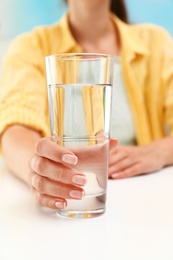 Photo of Woman holding glass of water at white table, closeup. Refreshing drink