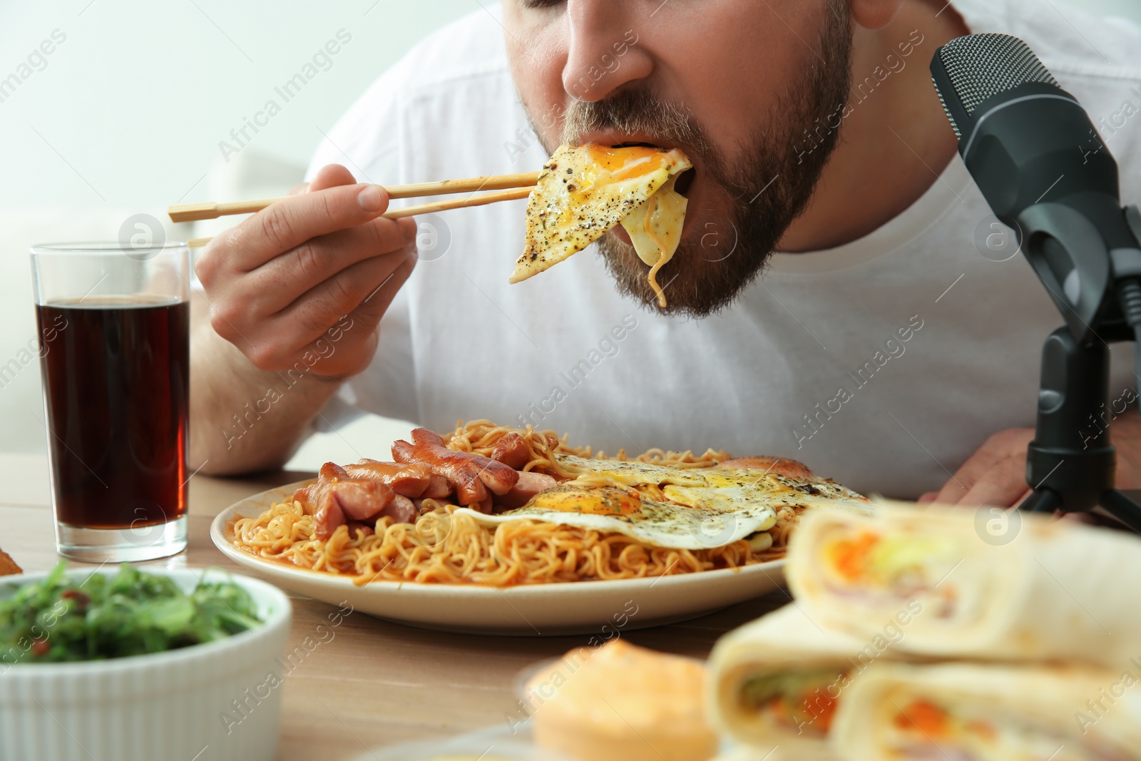 Photo of Food blogger eating in front of microphone at table, closeup. Mukbang vlog