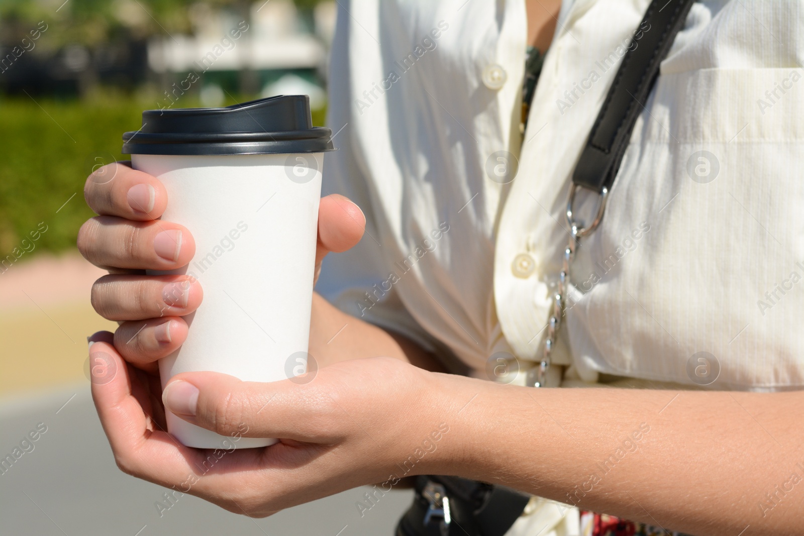 Photo of Woman holding takeaway coffee cup outdoors, closeup