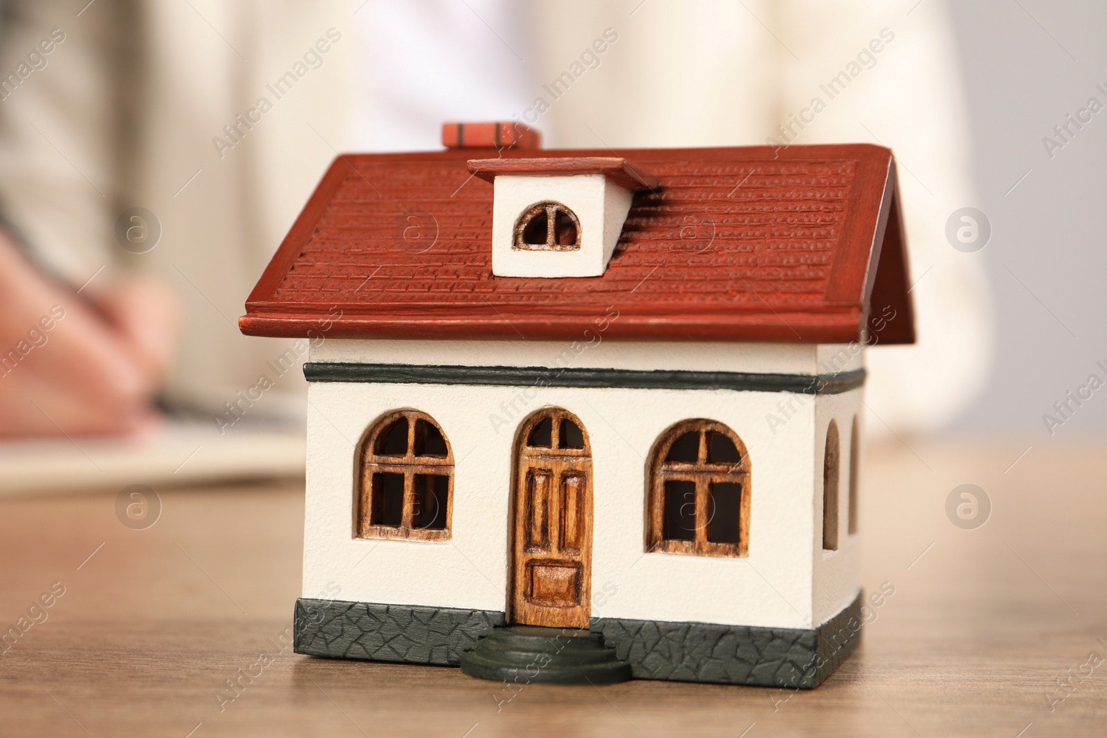 Photo of Mortgage concept. Woman writing at wooden table, focus on house model