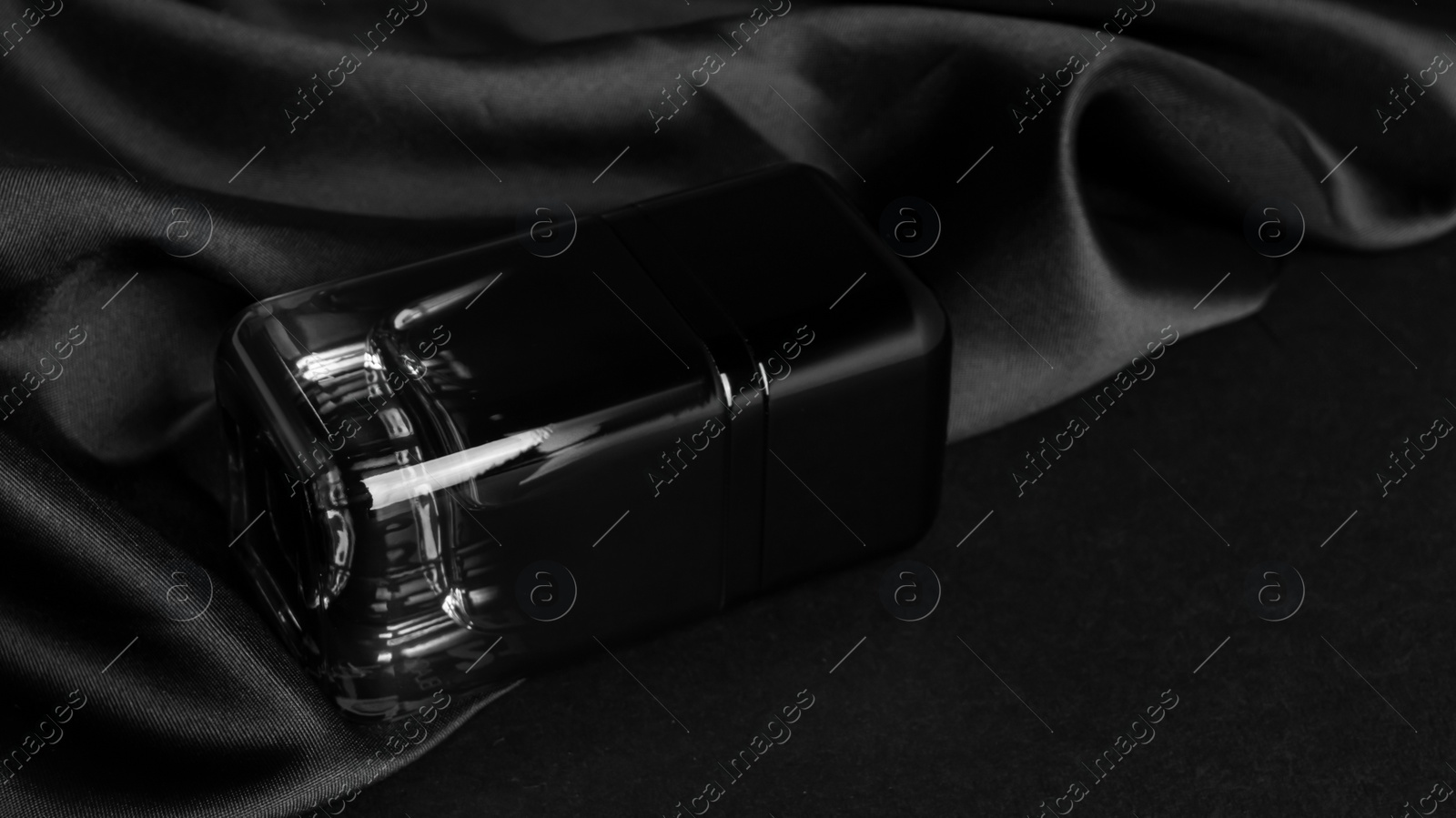 Photo of Bottle of luxurious perfume and silk fabric on black background, closeup