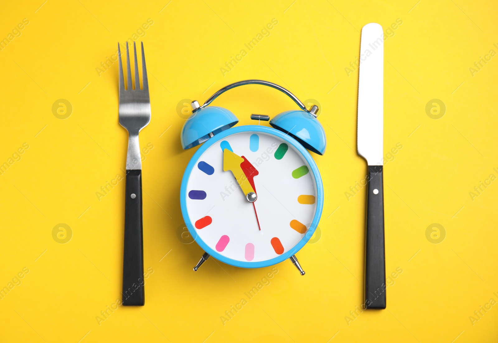 Photo of Alarm clock and cutlery on yellow background, flat lay. Diet regime