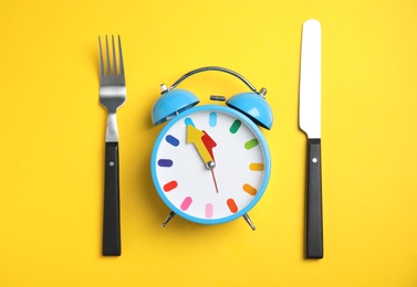 Alarm clock and cutlery on yellow background, flat lay. Diet regime