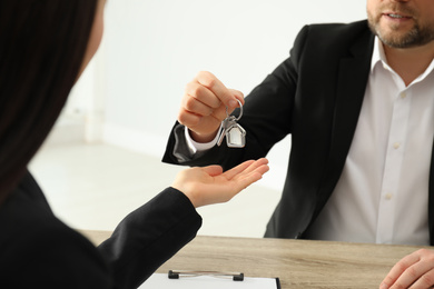 Real estate agent giving key to client at table in office, closeup