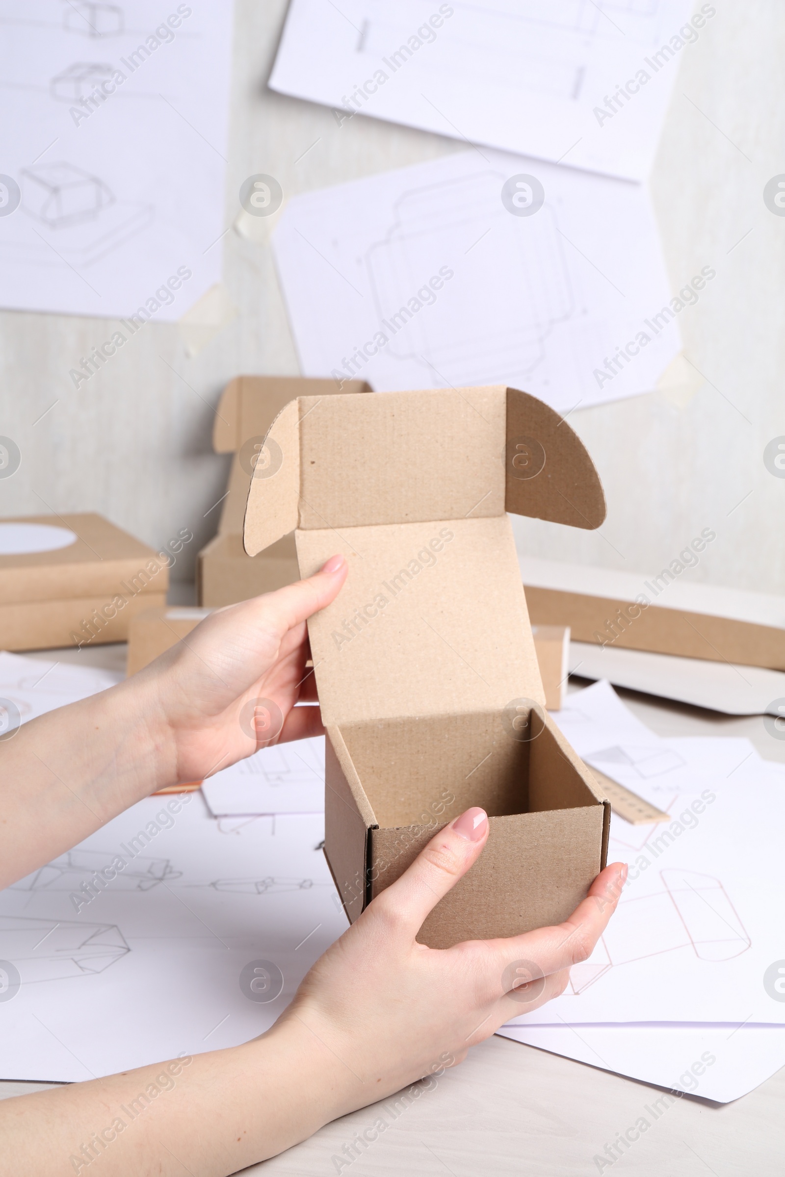 Photo of Woman holding cardboard box near drawings at table, closeup