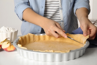 Photo of Woman cutting dough leftovers for traditional English apple pie in baking dish at white table, closeup