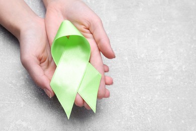 Photo of World Mental Health Day. Woman holding green ribbon on light grey background, closeup with space for text