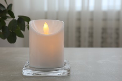Photo of Glowing decorative LED candle on grey table. Space for text
