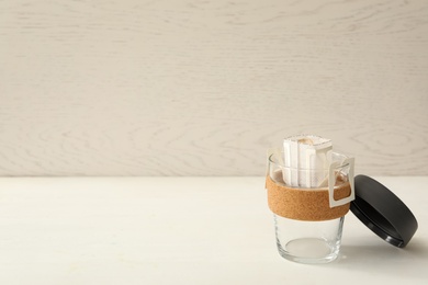 Photo of Drip coffee bag in glass cup on white table. Space for text