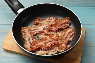 Photo of Delicious bacon slices in frying pan on blue wooden table, closeup