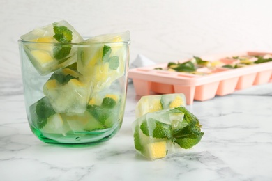 Photo of Mint and lemon frozen in ice cubes and glass on table