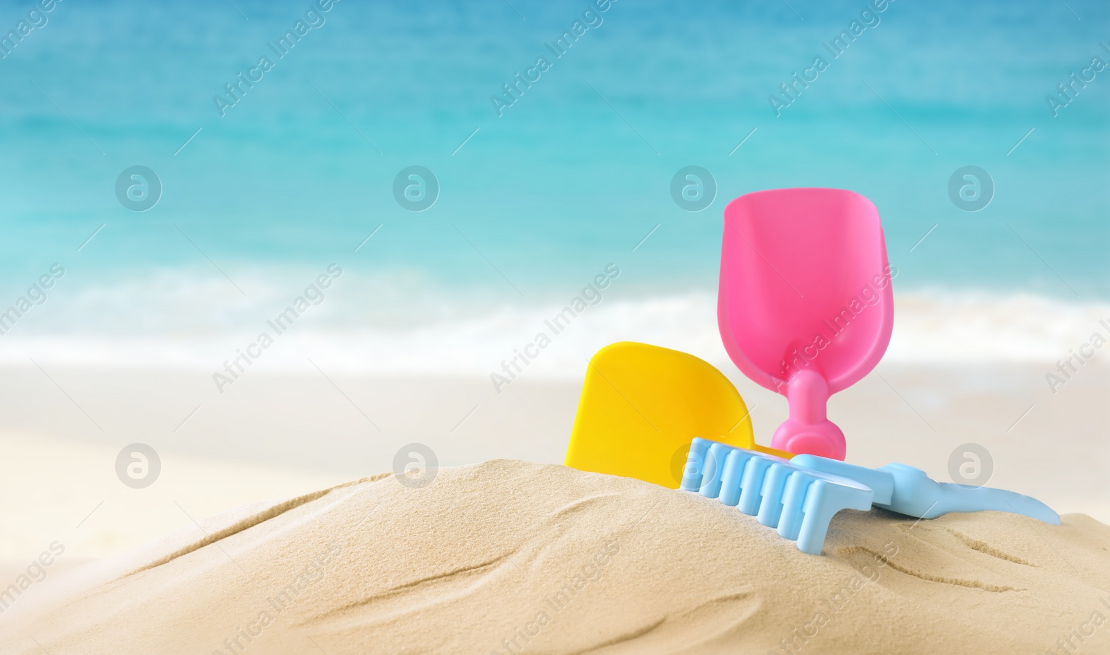 Image of Plastic toy set with shovel on sandy beach near sea, space for text 