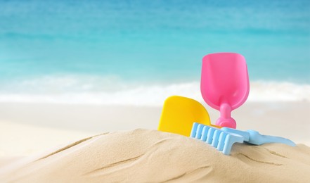 Image of Plastic toy set with shovel on sandy beach near sea, space for text 