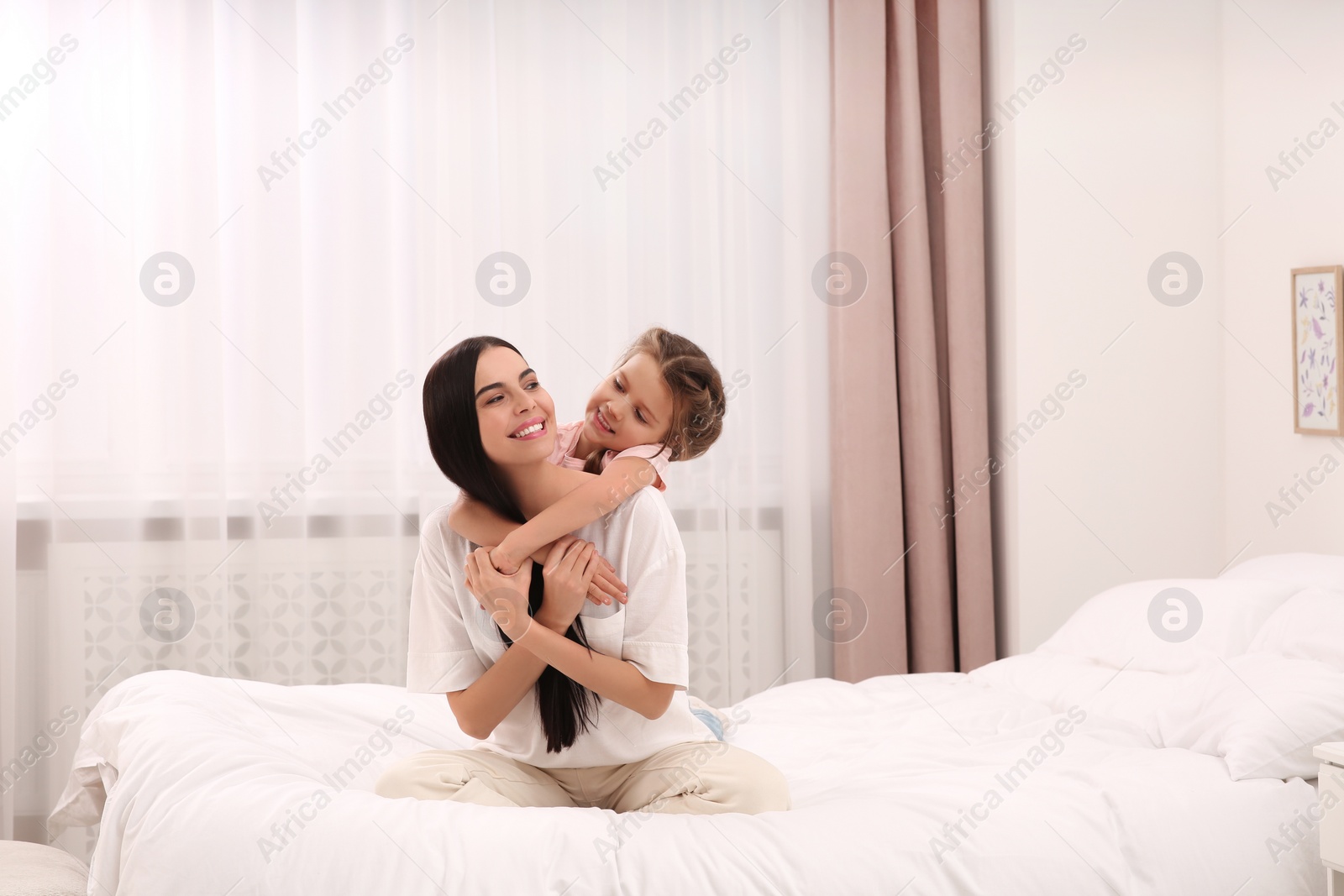 Photo of Happy woman and her daughter spending time together on bed at home, space for text. Mother's day celebration
