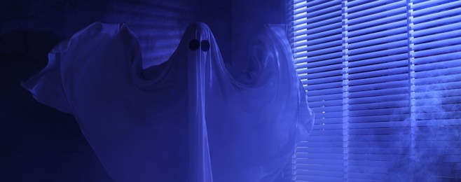 Creepy ghost. Woman covered with sheet near window in blue light