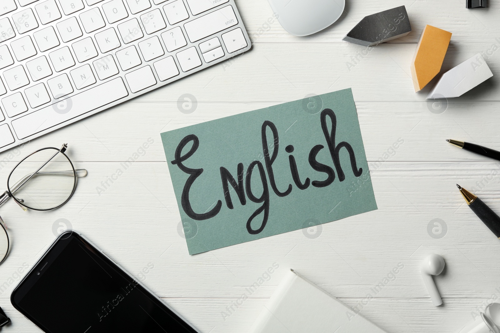 Photo of Sheet of paper with word ENGLISH, keyboard, smartphone and stationery on white wooden background, flat lay