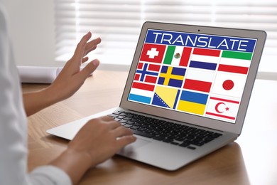 Image of Translator using modern laptop with images of different flags on screen at wooden table indoors, closeup