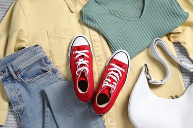 Photo of Pair of stylish red sneakers, clothes and bag on light grey fabric, flat lay