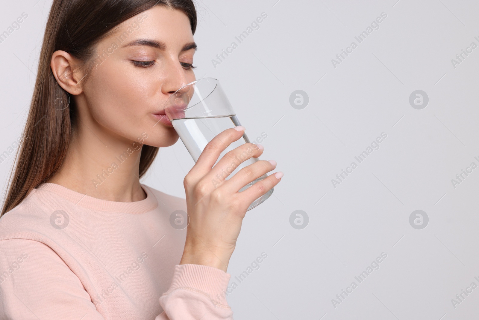 Photo of Healthy habit. Woman drinking fresh water from glass on light grey background. Space for text