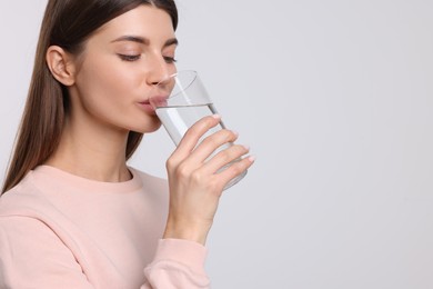 Photo of Healthy habit. Woman drinking fresh water from glass on light grey background. Space for text