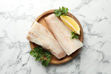Photo of Fresh raw cod fillets with parsley and lemon on white marble table, top view