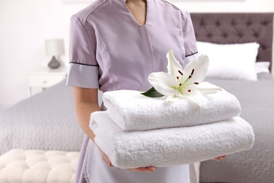 Photo of Maid holding fresh towels with flower in hotel room, closeup