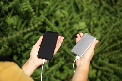 Photo of Woman charging smartphone with power bank in forest, closeup