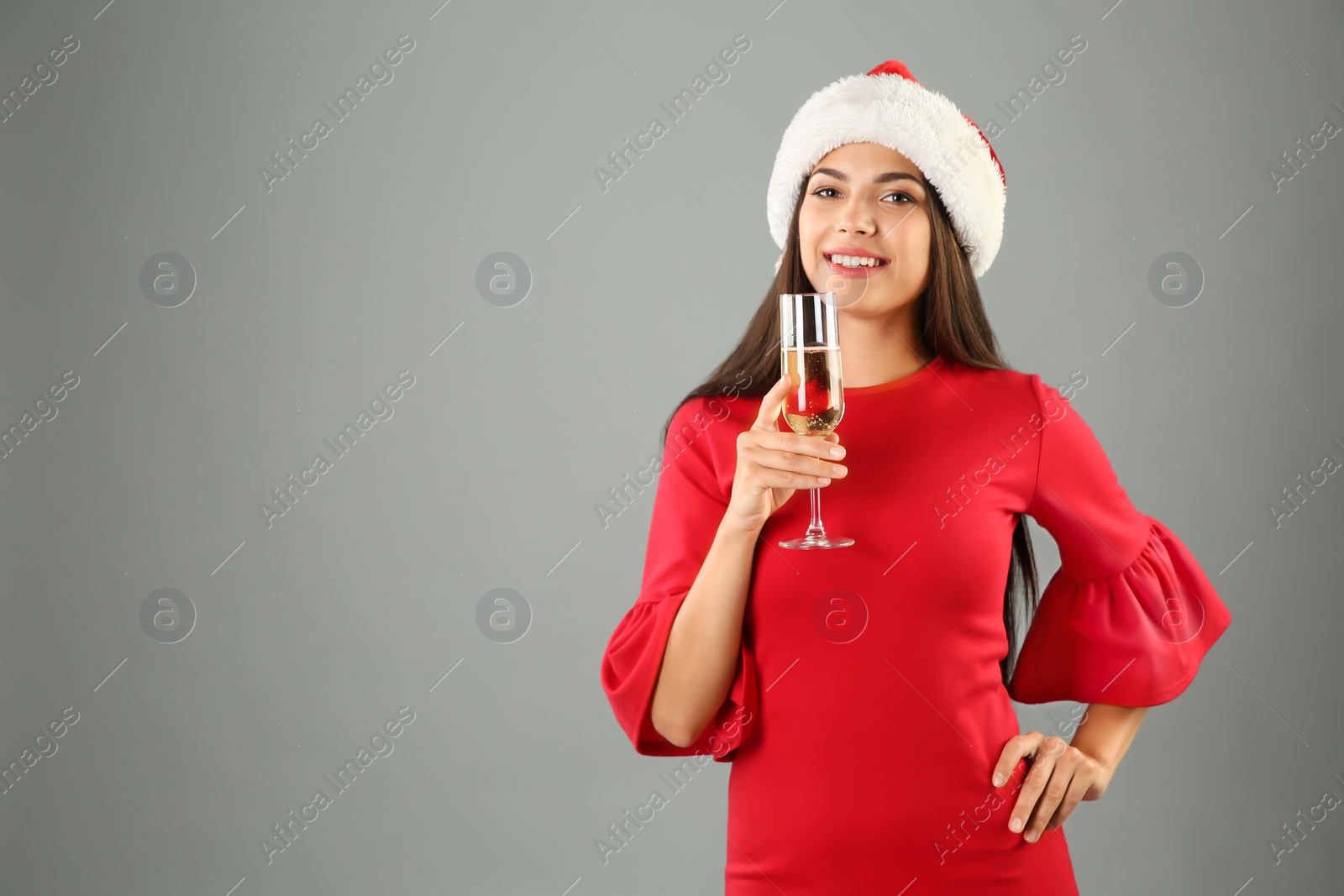 Photo of Young beautiful woman in Santa hat with glass of champagne on grey background. Christmas celebration