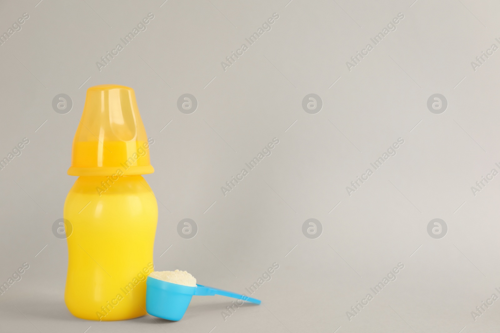 Photo of Feeding bottle with infant formula and scoop of powder on light grey background, space for text. Baby milk