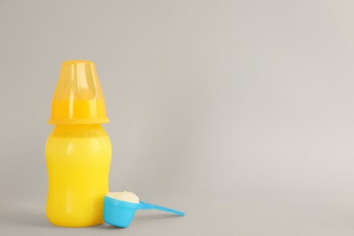 Photo of Feeding bottle with infant formula and scoop of powder on light grey background, space for text. Baby milk