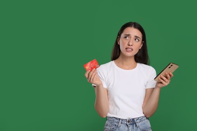 Confused woman with credit card and smartphone on green background, space for text. Debt problem