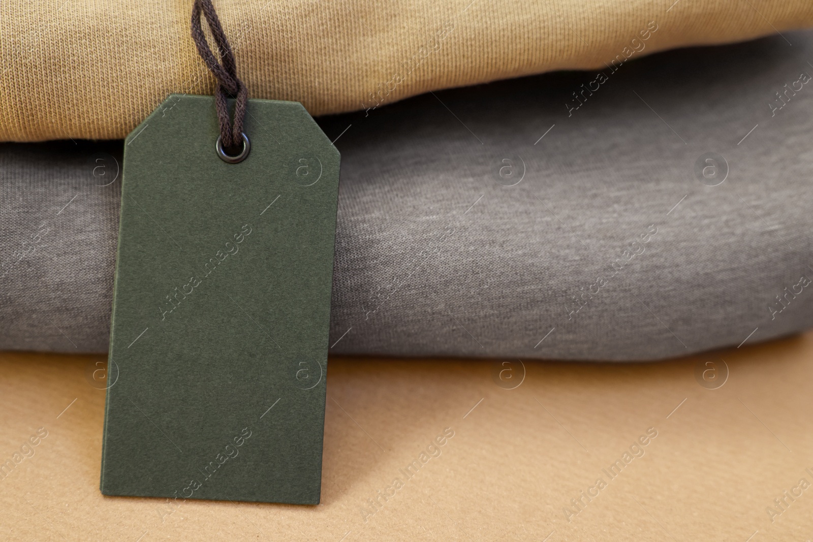 Photo of Garment with cardboard tag on kraft paper sheet, closeup. Space for text