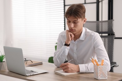 Man taking notes during webinar at wooden table indoors