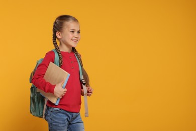 Happy schoolgirl with backpack and books on orange background, space for text