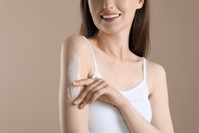 Photo of Woman applying body cream onto arm on beige background, closeup