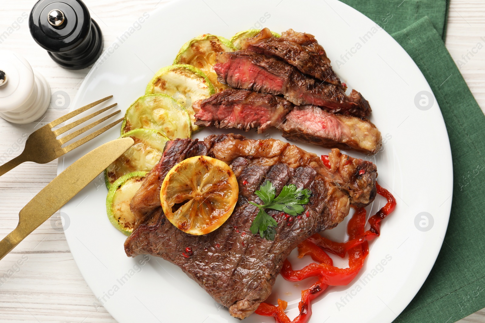 Photo of Delicious grilled beef steak and vegetables served on light wooden table, top view