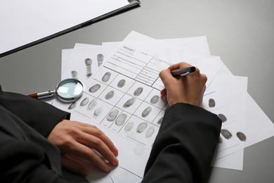 Photo of Female criminalist filling fingerprints card at table, closeup
